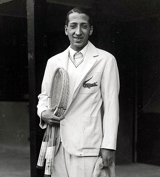 Photographie de René Lacoste avec ses raquettes et sa veste avec le crocodile brodé sur la poche. 