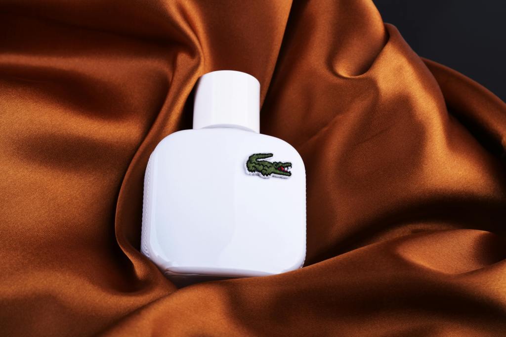 Flacon de parfum blanc sur lequel figure le crocodile emblématique de la marque Lacoste. 